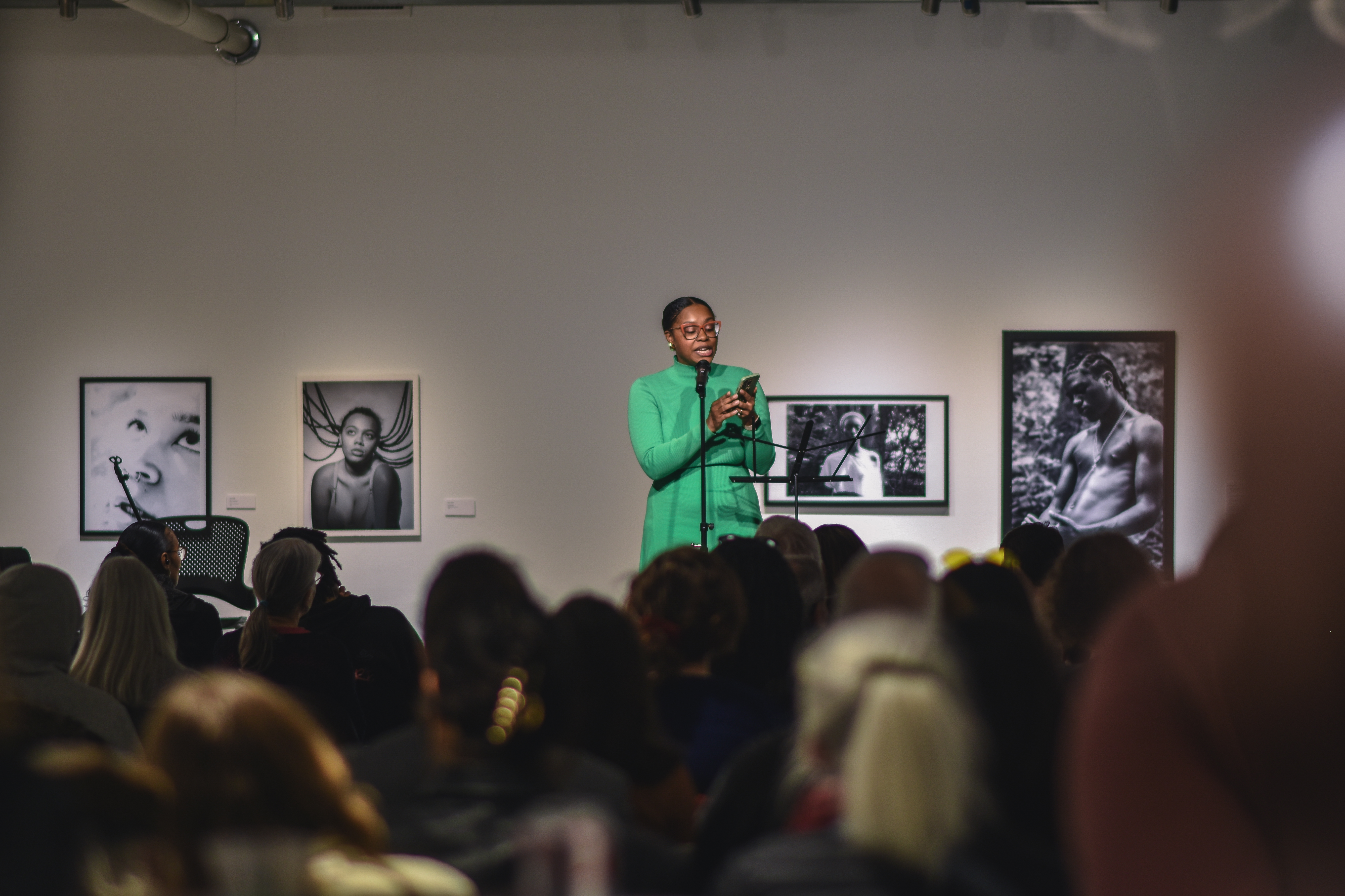 Ajanae in a green dress speaking to a crowd of people in the gallery