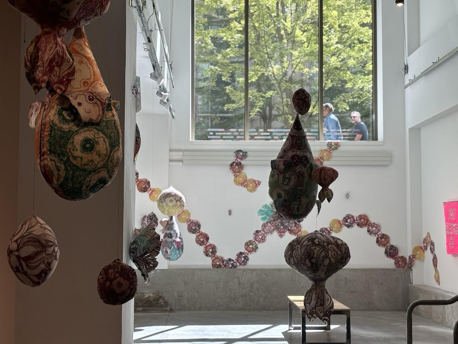 The lower gallery of UAS is filled with Alex McClay and Stephanie Berrie’s vibrant, hanging printmaking and sculpture work. The sculptures in the foreground are covered in shadow whilst the background is illuminated by natural sunlight