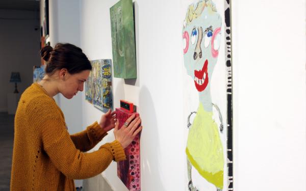 An intern hangs a painting on a wall.